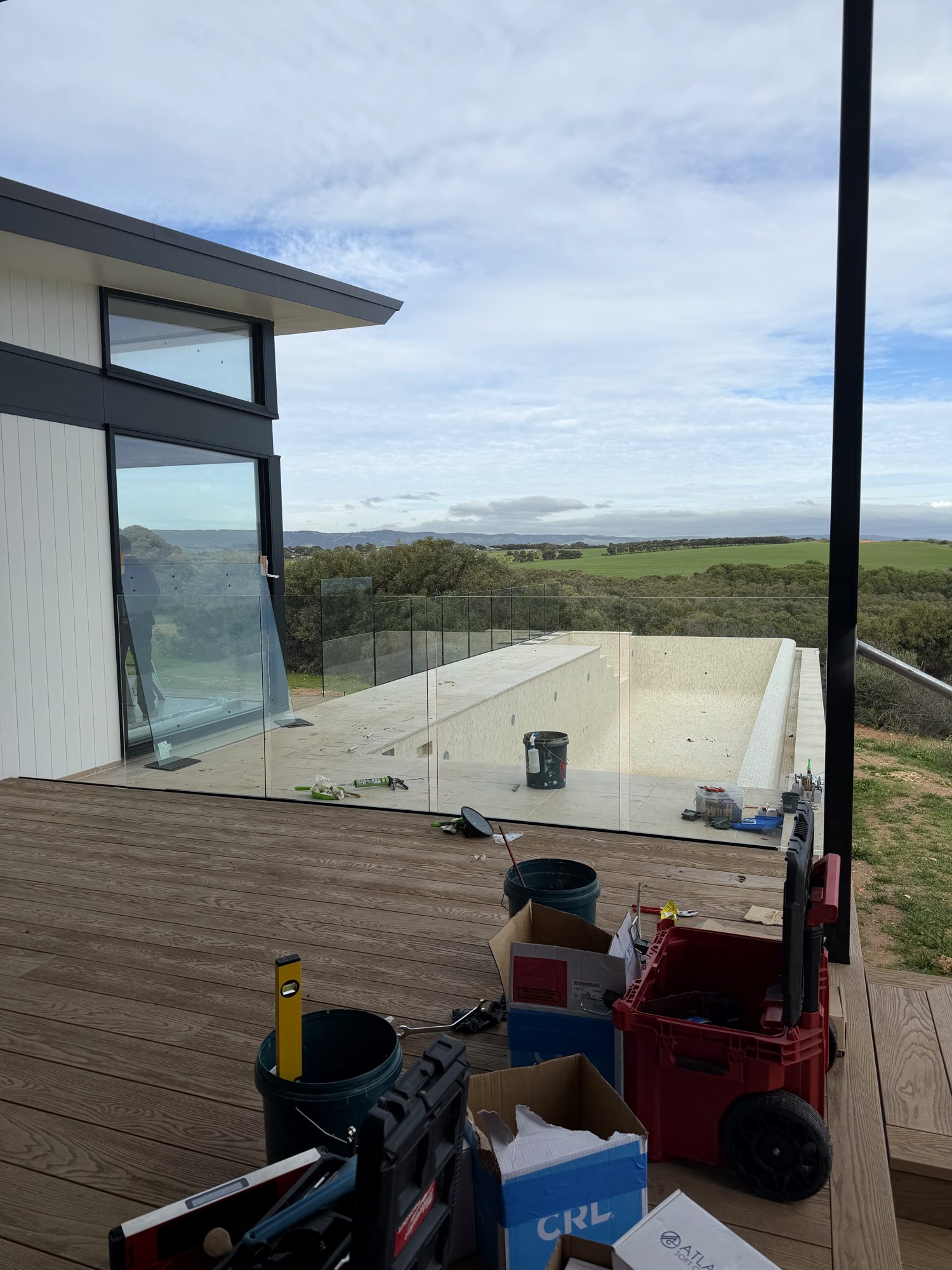 UGS mid-installation — frameless glass balustrade on a hillside deck overlooking open country, South Australia